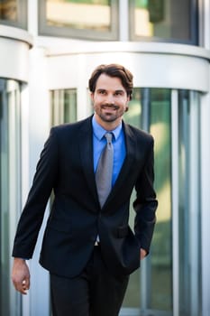 Young trendy businessman in front of a business building successfully with beard and dark hair