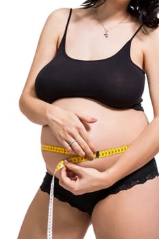 Pregnant woman with a measuring tape measures her girth on her abdomen isolated against a white background
