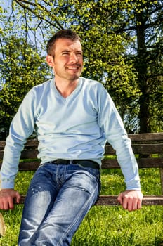 attractive man is relaxing on a bench in a natural environement