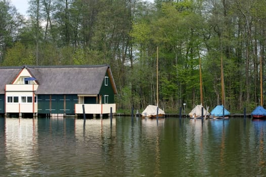 Photograph of houses with boat sheds and sailboats on a lake.