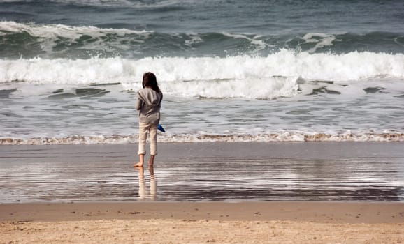 Young girl stands for a moment looking out at the ocean waves crashing in