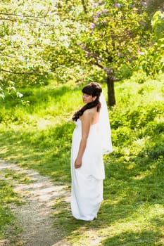 Beautiful brunette bride walking on path under trees at park