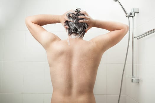 Photo of from back of muscular man washing head at shower