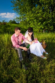 Young groom opens champagne at picnic in park