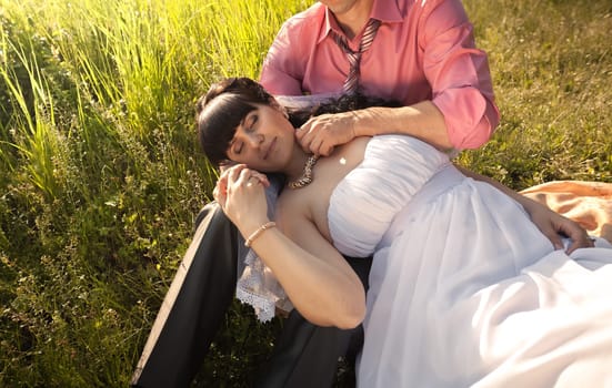 Closeup portrait of bride sleeping on grooms knees at field