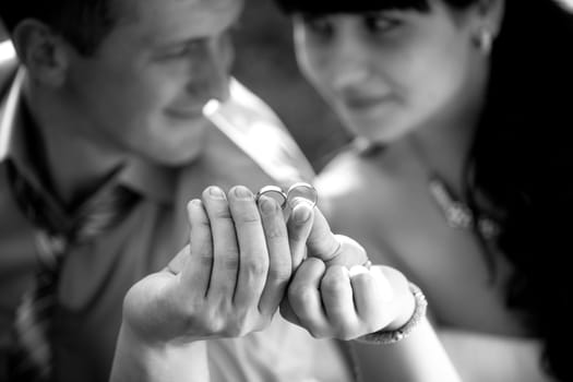 Black and white portrait of newly married couple holding wedding rings at park