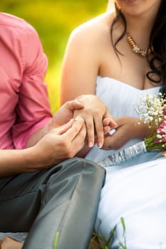 Closeup photo of groom putting golden ring in brides hand at park