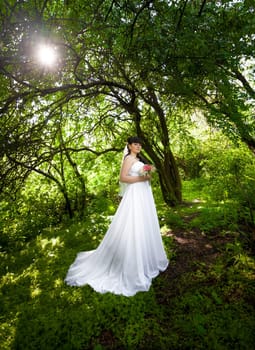 Beautiful bride in long dress under big trees at old forest