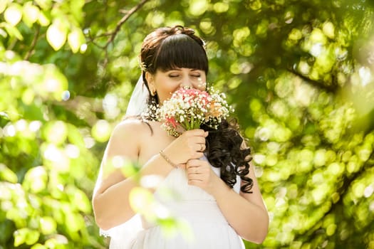 Closeup portrait of young brunette bride sniffing wedding bouquet at park
