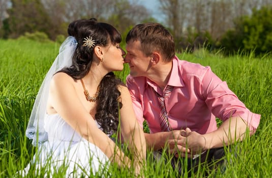 Portrait of bride and groom kissing in lips while sitting on meadow
