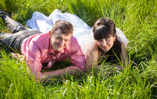 Portrait of smiling bride and groom lying on field at summer