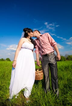 Beautiful bride and groom holding picnic basket and kissing at field