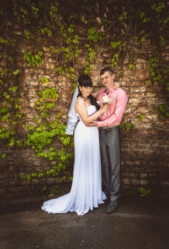 Newly married couple hugging against old brick wall