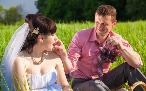 Closeup portrait of groom feeding bride with grapes at picnic