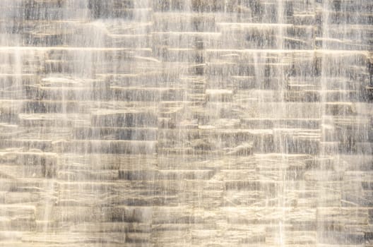 Falling water stream against stone wall rough texture with night backlight
