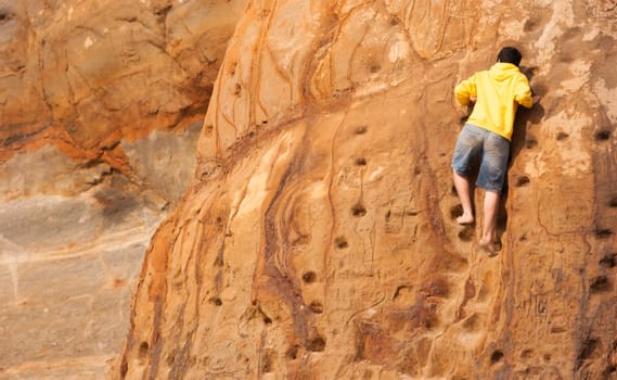 Young man in shorts and yellow sweatshirt climbing sandstone wall