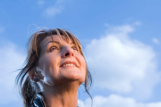 Side close-up of a middle-aged woman dreamily looking up into the blue sky
