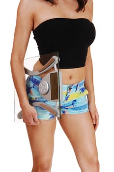 A closeup picture on the mid section on a young woman in shorts, holding.a scale under her arms, isolated on white background..