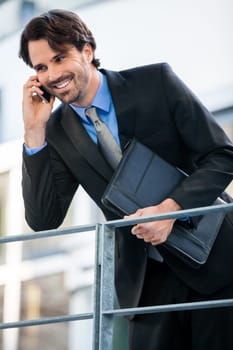 Young trendy successful businessman with mobile phone smartphone cheerful lyrane in front of an outdoor business building