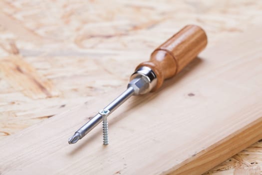 Close-up of a cross screwdriver with screws in wood while DIY in a workshop