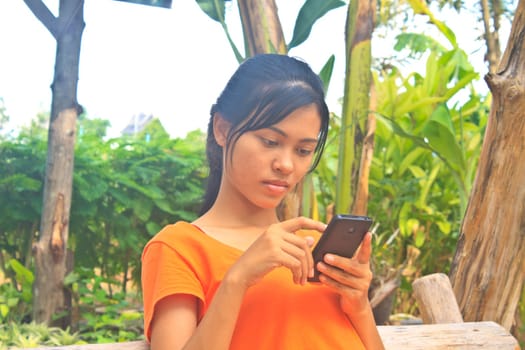 Young girl sitting on the wooden swing along with mobile phone