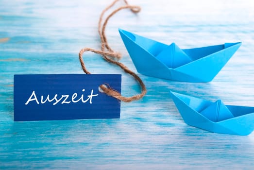 Two Origami Boats with a Label with the German Word Auszeit which means Downtime