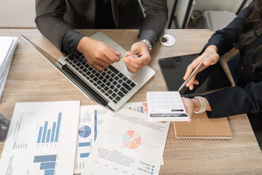 Close-up view of diverse business professionals reviewing financial reports and utilizing a calculator while discussing strategies in an office environment.