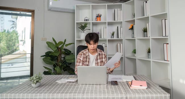 A focused young professional reviews financial documents and uses a calculator in a contemporary office setting.