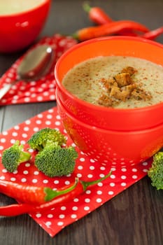 Soup bowl with broccoli soup with fresh pepper and chilli close-up on a wooden table