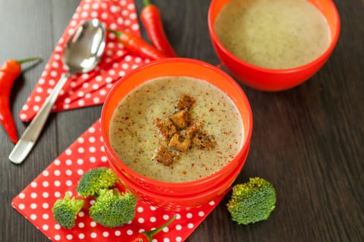 Soup bowl with broccoli soup with fresh pepper and chilli close-up on a wooden table