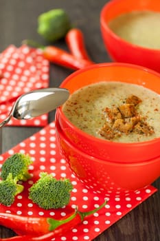 Soup bowl with broccoli soup with fresh pepper and chilli close-up on a wooden table