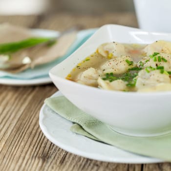 Bowl with Russian Pelmeni Italian tortellini with broth and parsley close-up on a wooden table