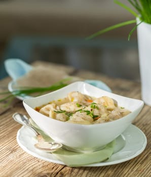 Bowl with Russian Pelmeni Italian tortellini with broth and parsley close-up on a wooden table