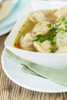 Bowl with Russian Pelmeni Italian tortellini with broth and parsley close-up on a wooden table