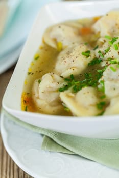 Bowl with Russian Pelmeni Italian tortellini with broth and parsley close-up on a wooden table