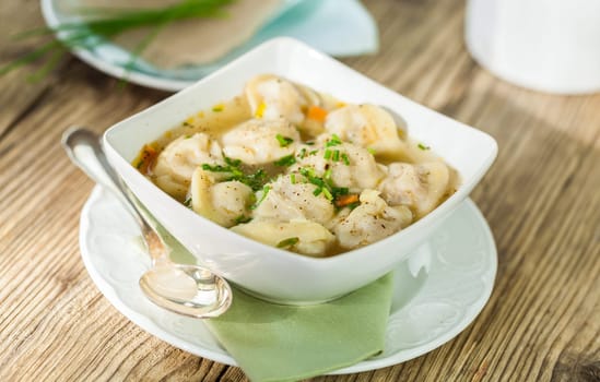 Bowl with Russian Pelmeni Italian tortellini with broth and parsley close-up on a wooden table