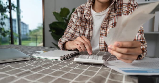 A young man reviews cash and uses a calculator for budgeting at home, emphasizing financial management and planning.
