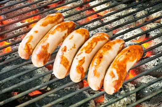 Six roast sausages on a large charcoal grill
