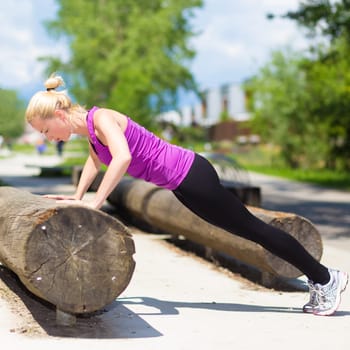 Young spotry woman does pushups outdoors in the park.