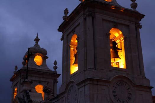 A spooky and dark church bell tower with the bells lit up by lights on the inside.