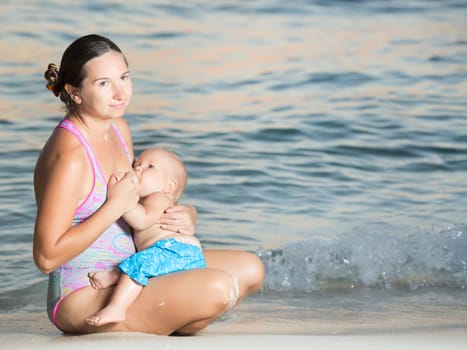 Mother breastfeeding baby on the beach at sunset