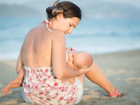 Mother breastfeeding baby on the beach
