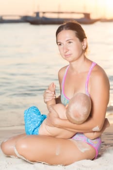 Mother breastfeeding baby on the beach at sunset
