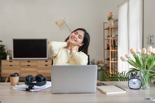 A young woman gently massages her neck while sitting at her desk, showcasing the importance of self-care in a work-from-home setting.