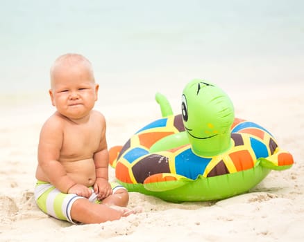 Baby sitting om the beach with swim ring