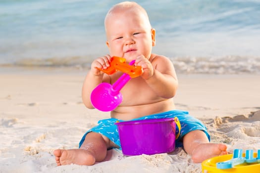 Cute baby on the tropical beach playing toys
