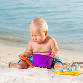 Cute baby on the tropical beach playing toys