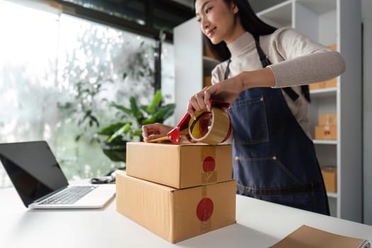 A young woman applies tape to boxes in a modern office, showcasing her packaging skills and organizational abilities.