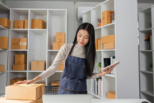 A young woman organizes packages in a contemporary workspace, using a notebook to manage inventory efficiently.