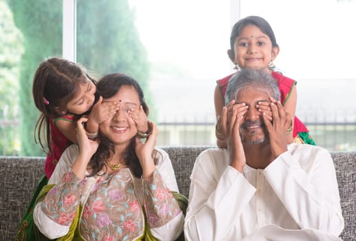 Indian family living lifestyle at home. Cute girls in traditional sari costume covering father and mother eyes. Asian parents and children.